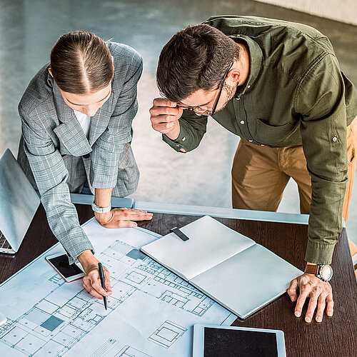 As part of project implementation, BIRKHOLZ+ monitors all measures, accepts completed services, and manages defect tracking. Photo: BIRKHOLZ+, https://birkholzplus.com/wp-content/uploads/Birkholz-Leistungen-Projektrealisierung.jpg Two BIRKHOLZ+ employees reviewing a technical plan together as part of project implementation