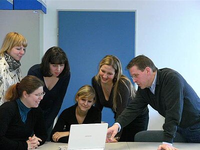 Estudiantes y un profesor del TH Wildau observan un PC con el software de gestión de proyectos Projektron BCS.