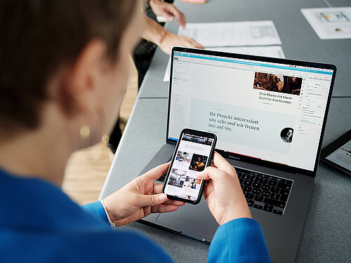 Eine Mitarbeiterin von Stämpfli Kommunikation ruft Webinhalte mit dem Smartphone und Laptop auf. 